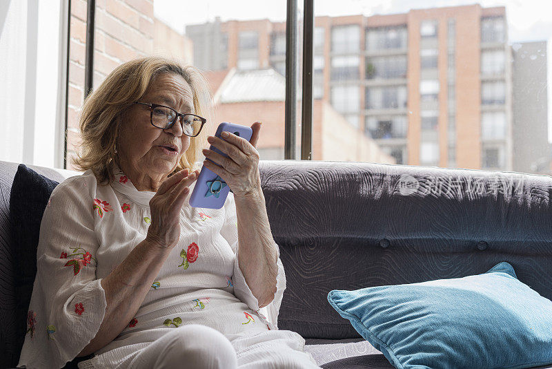 奶奶在家里的沙发上用手机和她的朋友和家人通过视频通话