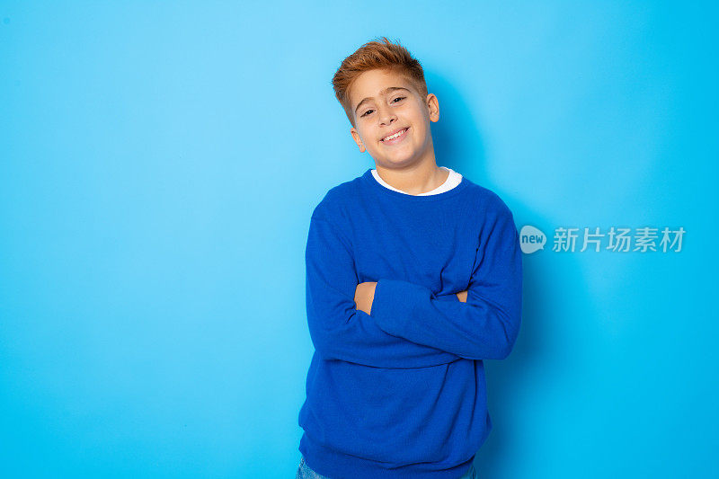 红头发的男孩双臂交叉，幸福的脸孤立在蓝色的背景。