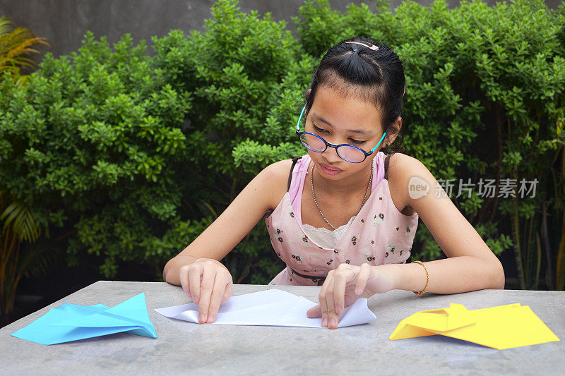 一个戴着眼镜的年轻泰国女孩正在折叠纸飞机