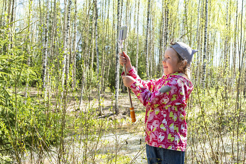一个白人小孩在春天的森林里散步。一个5岁的小女孩用手机拍照片和视频。