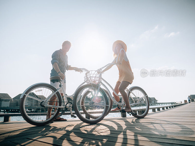 一对骑着自行车的夫妇在马尔代夫的木制码头上凝视着田园诗般的风景