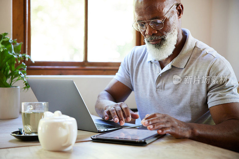 一个成熟的男人坐在咖啡馆里用平板电脑和笔记本电脑在线工作