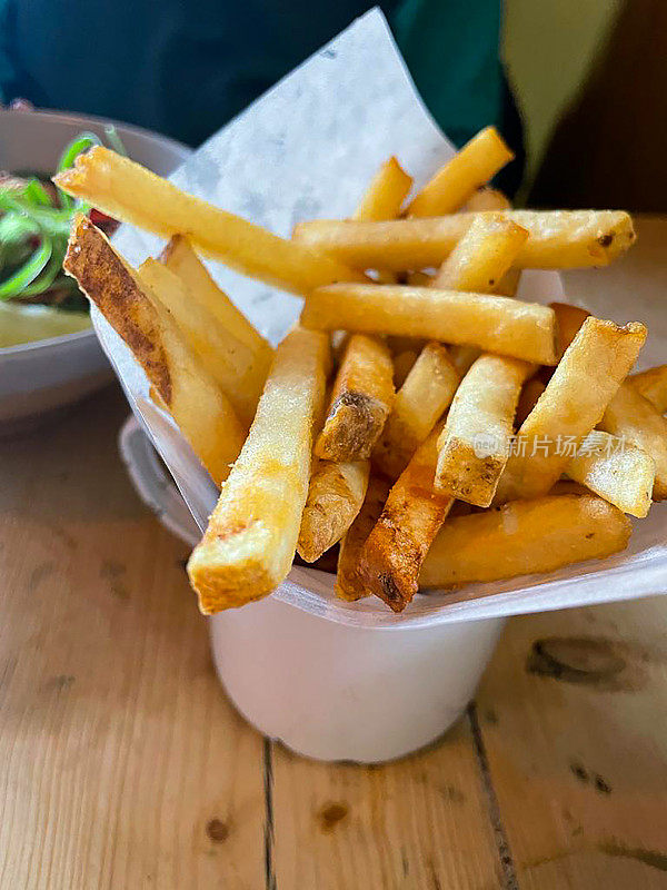 餐厅场景的特写图像，餐桌上有一碗白色的味增鲑鱼面和配菜炸薯条在珐琅杯，在背景中难以辨认的人，升高的视野，重点放在前景