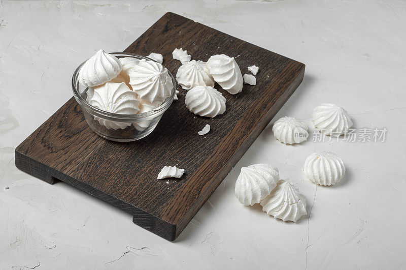 法式蛋白霜甜点放在灰色背景的深色木板上的玻璃碗里。到处都是完整的和破碎的蛋白酥皮。