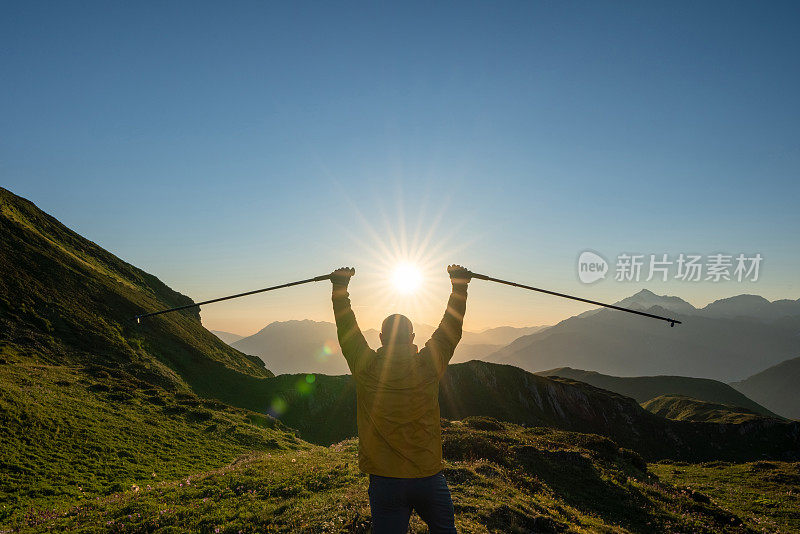 后视图徒步者独自站在山上，举着徒步杆在日落