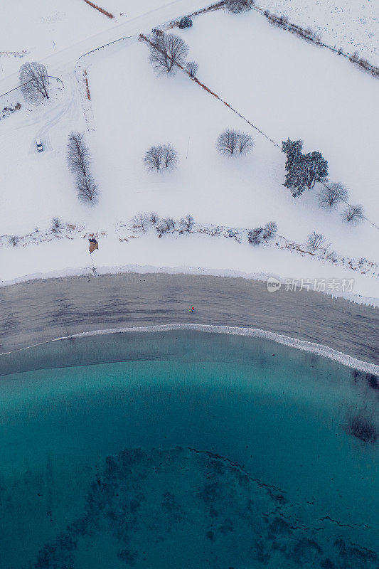 航拍图像的女人和男人走在风景秀丽的turqouse海滩在雪与山景在挪威