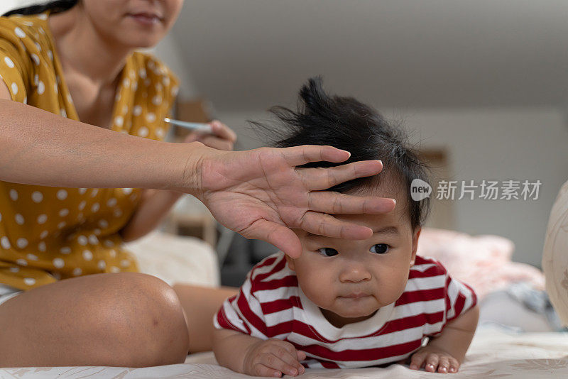 年轻的亚洲母亲照顾和使用数字体温计和手检查体温她的儿子在疾病期间流感发烧。家庭宝宝生活方式照顾和保健理念。