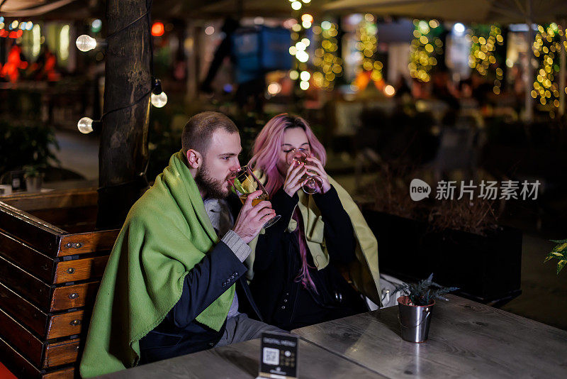 在一个寒冷的夜晚，一对浪漫的相爱的年轻夫妇坐在一家餐馆里，披着毯子喝着啤酒。