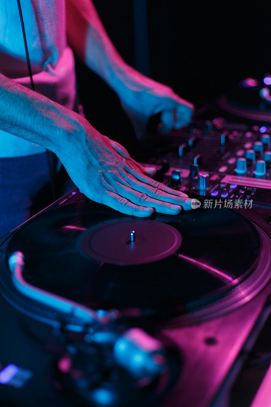 嘻哈DJ在明亮的霓虹灯下在唱盘上刮黑胶唱片。手专业的唱片骑师刮碟上转盘播放器