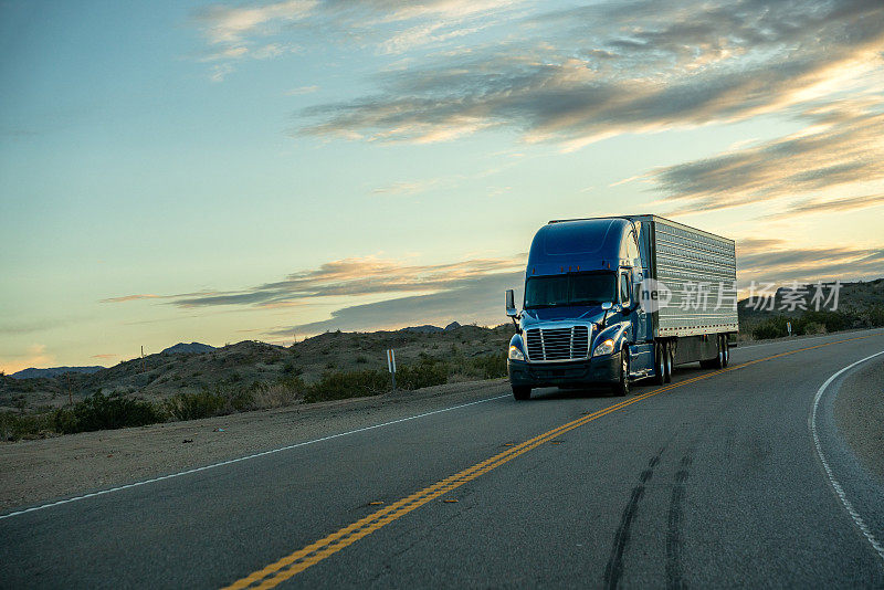 一辆蓝色的半挂式卡车行驶在双车道公路上，日落时分美丽的云雾缭绕