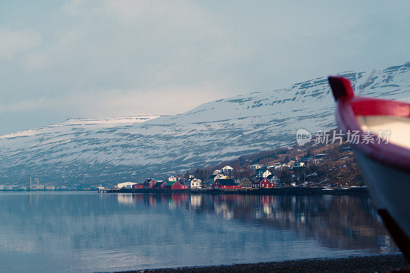 在日出时，在一个湖和一个美丽的冰岛村庄前的岸边的船