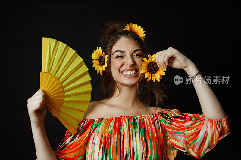 微笑着的年轻女子，头发上插着向日葵，手里拿着一把黄色的扇子