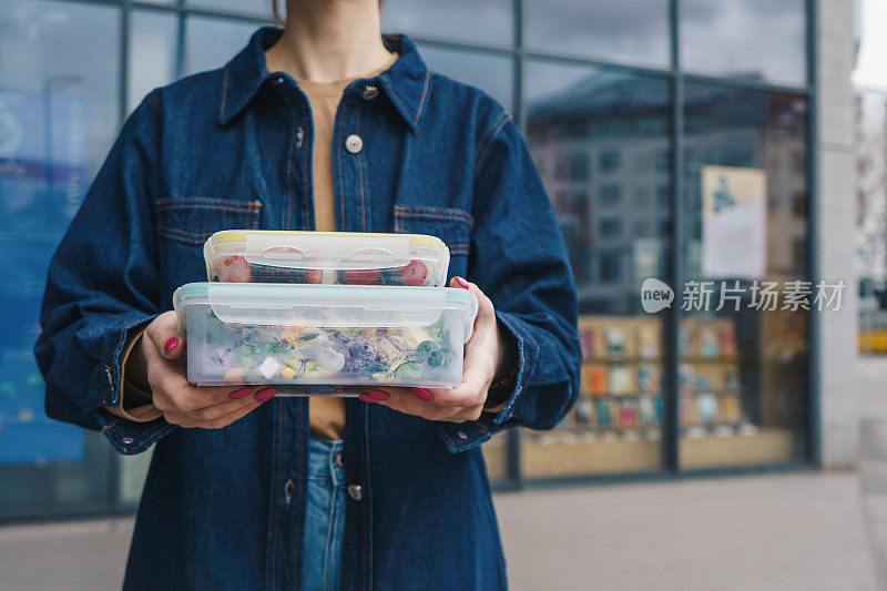 一名妇女在户外拿着可重复使用的塑料容器，里面装着沙拉和零食