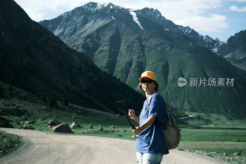 开朗的成熟女性背包客在天山的高地路上拍摄视频