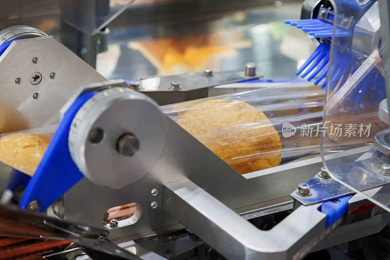 在面包制造厂的生产线上，食品级塑料袋里的烤面包在传送带上移动到包装机中密封。食品加工及工业概念。