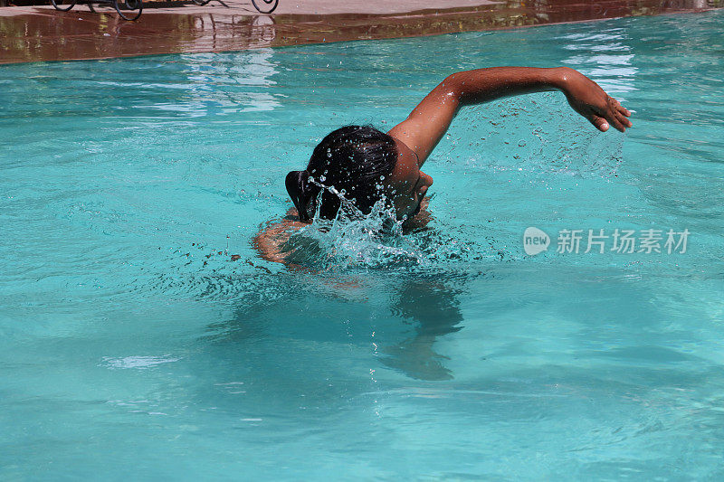 印度男子在清澈的水中做前爬的特写，室外，游泳池，绿松石蓝色马赛克瓷砖被波纹水扭曲，游泳和飞溅，波涛汹涌的水面反射，重点放在前景