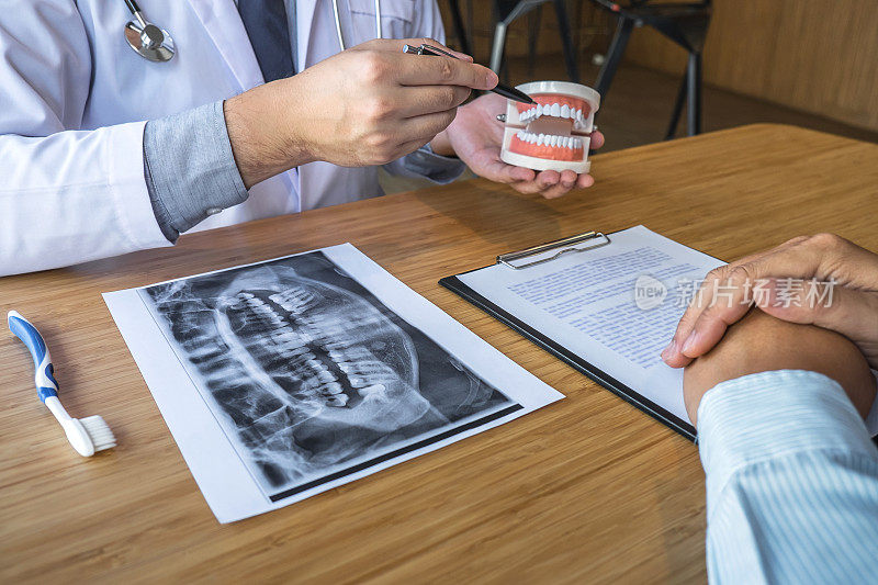 专业牙医与患者讨论颌骨和牙齿的x光照片，同时解释会诊治疗问题，并在便签本上记录病史