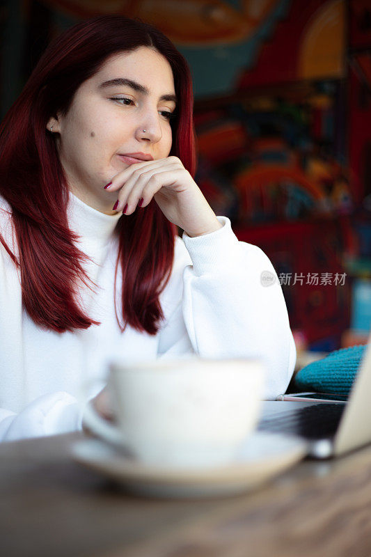 年轻的红发女学生正在咖啡店学习。