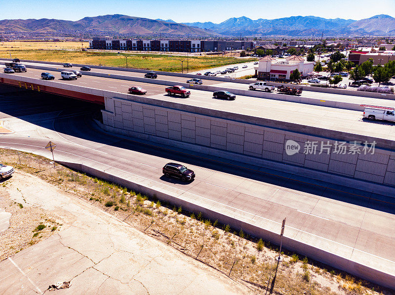 从空中俯瞰，在一个闷热的夏日，熙熙攘攘的高速公路上，汽车、卡车、suv和半面包车在远处高耸的山脉下穿行。