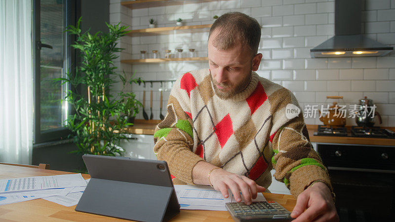 成年男性坐在厨房用笔记本电脑支付账单，用计算器计算费用，做预算控制，管理财务，审查逾期贷款