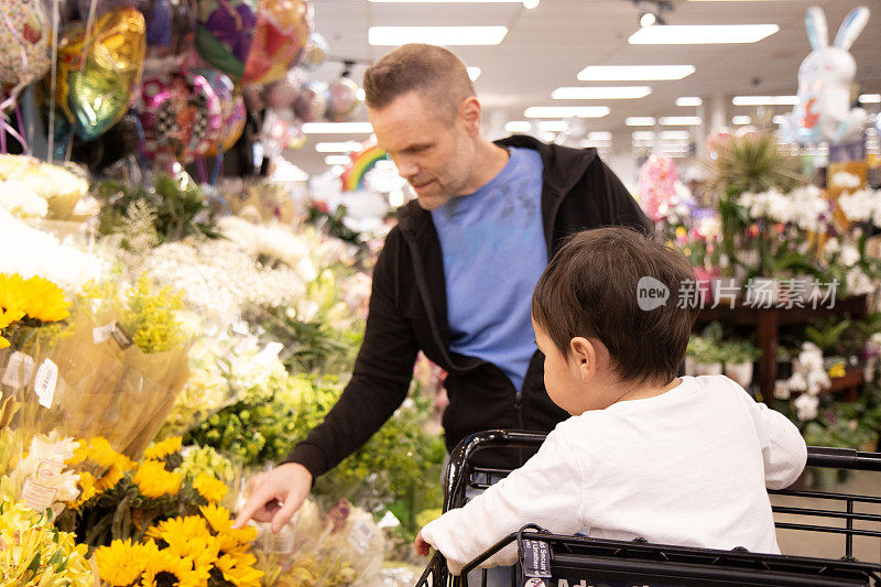 爸爸和蹒跚学步的儿子在杂货店为妈妈挑选鲜花
