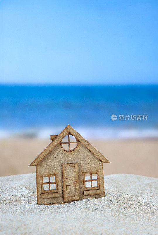 在沙滩上的木质镂空模型度假小屋图像，沙滩背景与退潮时的海浪，大海和海岸线，重点放在前景，度假租赁和度假屋的概念，复制空间