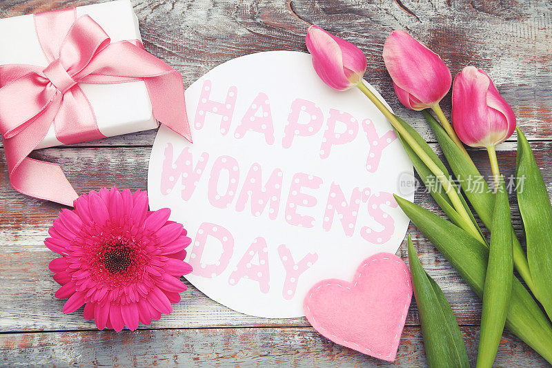 非洲菊和郁金香花，心，礼盒和木制背景的圆形卡片，上面写着妇女节快乐