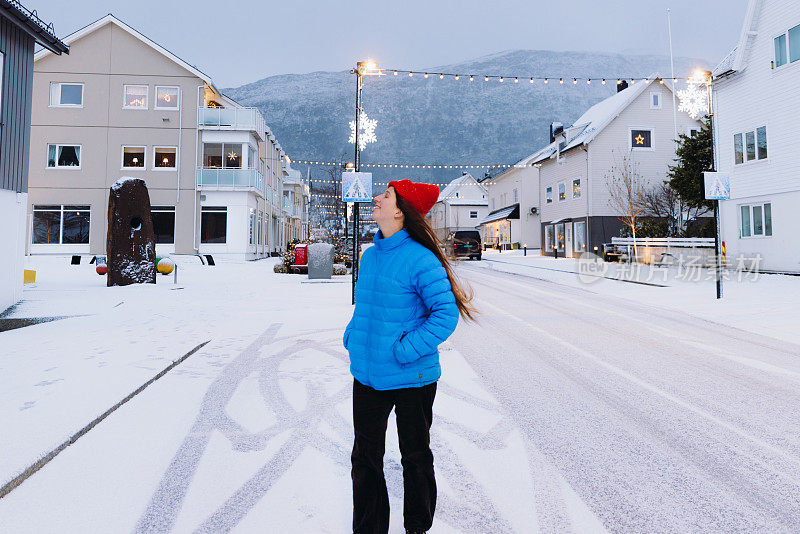 穿着蓝夹克和红帽的快乐女人在挪威城市思考冬天的时间