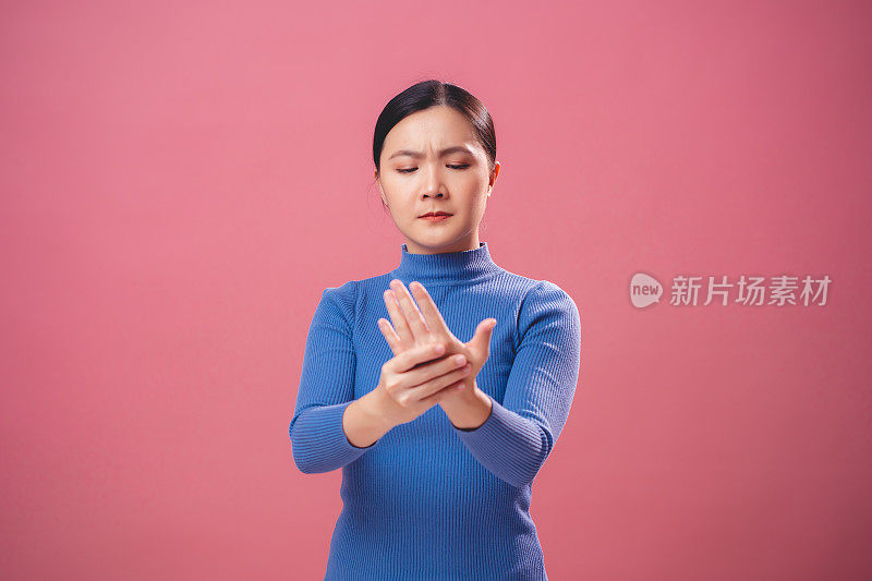 一名亚洲女性因手部疼痛而孤立地站在粉红色的背景上。