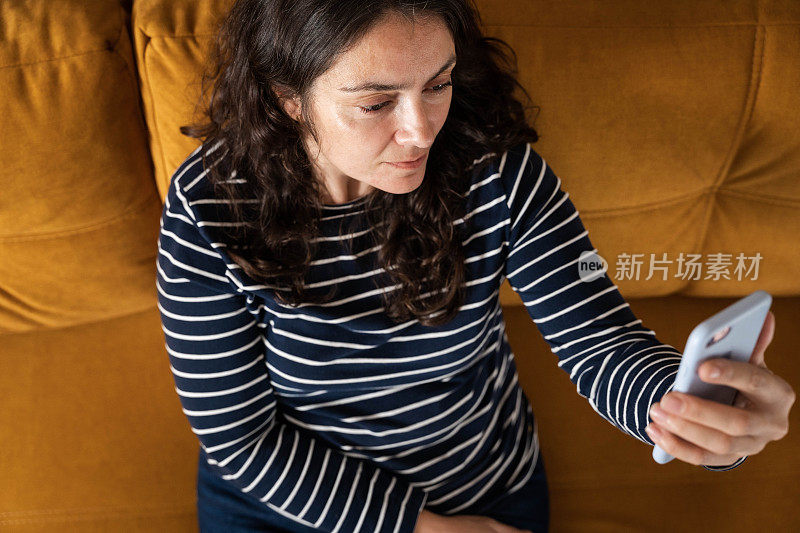 中年妇女舒舒服服地坐在沙发上，用智能手机打视频电话