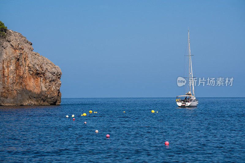 岬角对面有一艘孤零零的游艇;海里有许多五颜六色的浮标。晴天，碧蓝透明的大海。西班牙巴利阿里群岛的马略卡岛