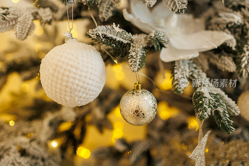 近距离观察美丽的冷杉树枝上闪闪发光的白色小玩意或球，金色的圣诞装饰品和灯。节日的背景。圣诞树上的装饰。喜庆新的2024年。副本的空间。