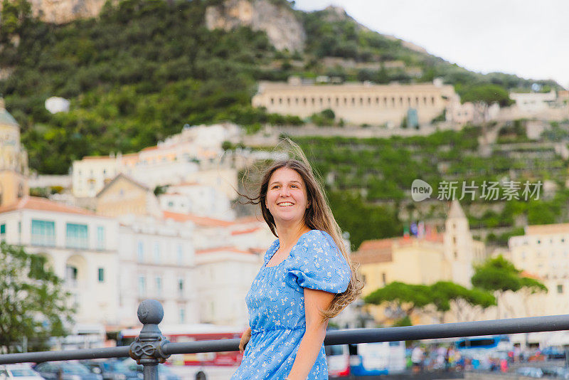 穿着蓝裙的快乐女子在海港漫步，欣赏阿马尔菲的美景
