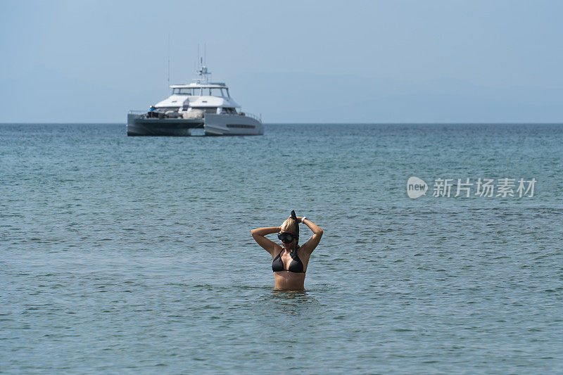 在希腊的夏日大海里，一个穿着泳装的小女孩正在一艘游艇附近浮潜。