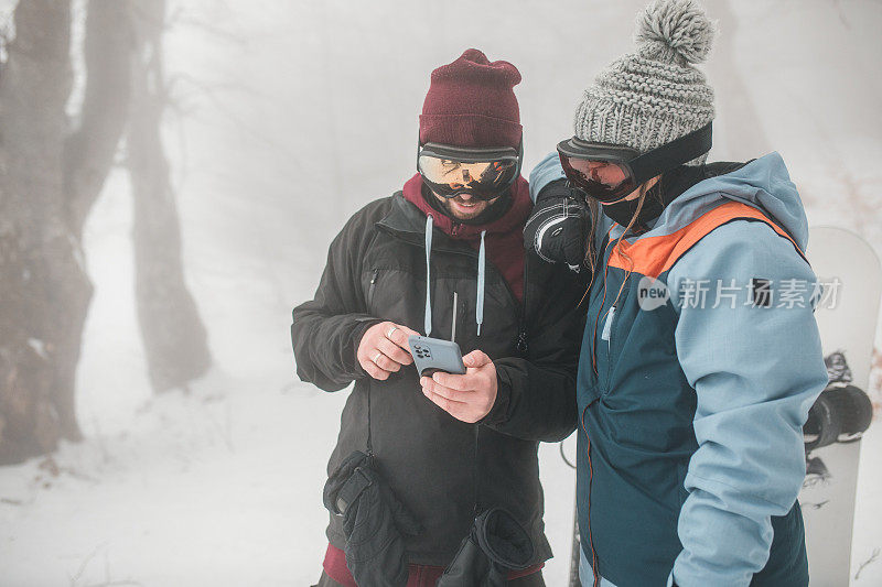 一名男子和一名女子在山上用手机追踪他们需要滑下滑雪板的位置