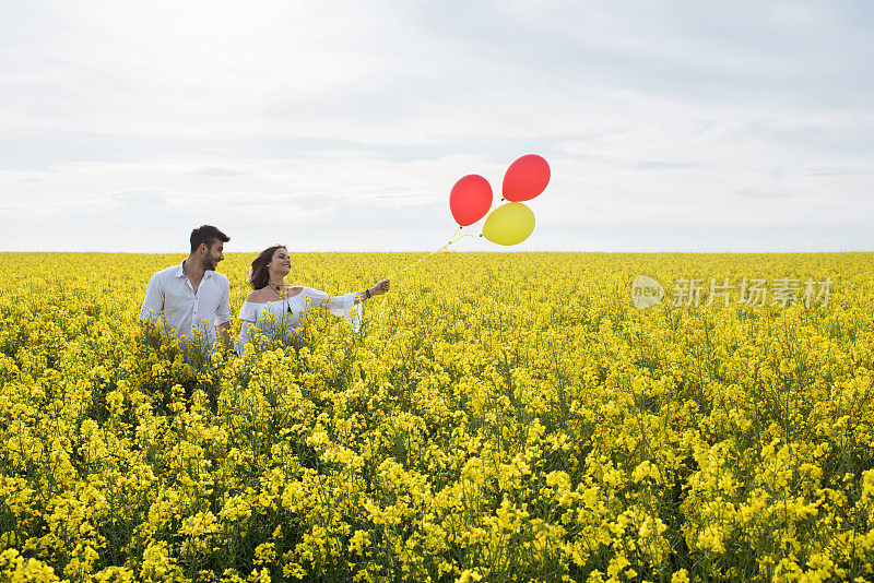 年轻幸福的夫妇拿着彩色气球走过鲜花田。