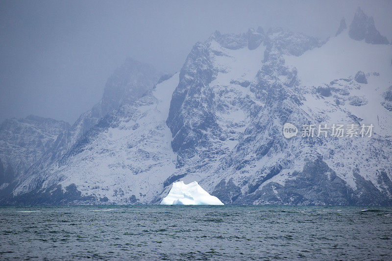 一座白色的冰山耸立在深蓝色和朦胧的冰川中