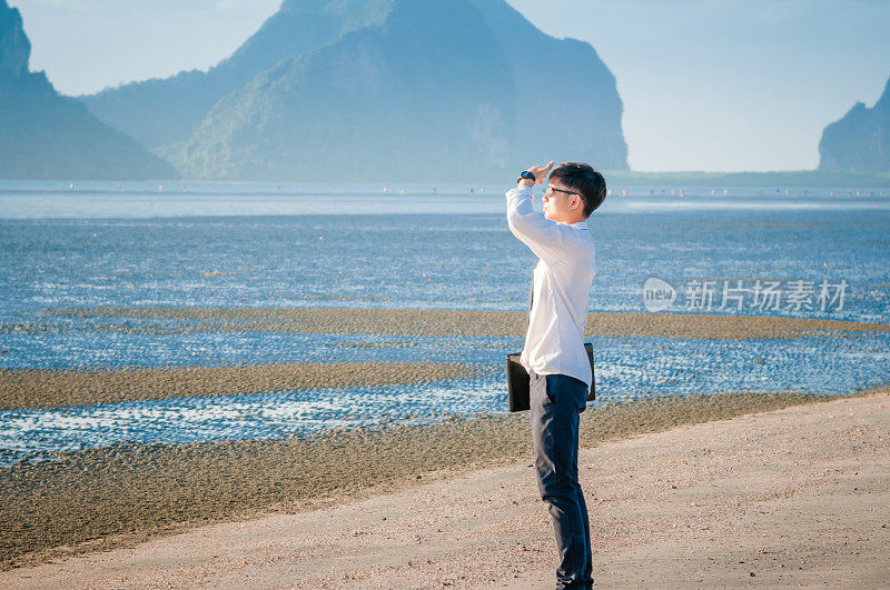 亚洲商人放松在海滩上使用笔记本电脑和智能手机