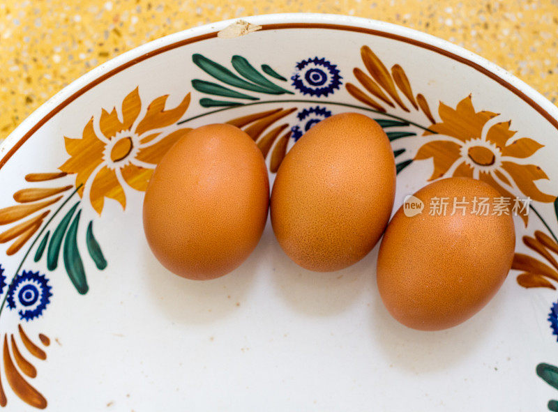三个棕色的鸡蛋在一个彩色的古董陶瓷碗