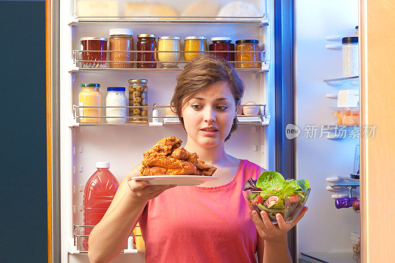 女人在打开的冰箱中选择健康或不健康的零食