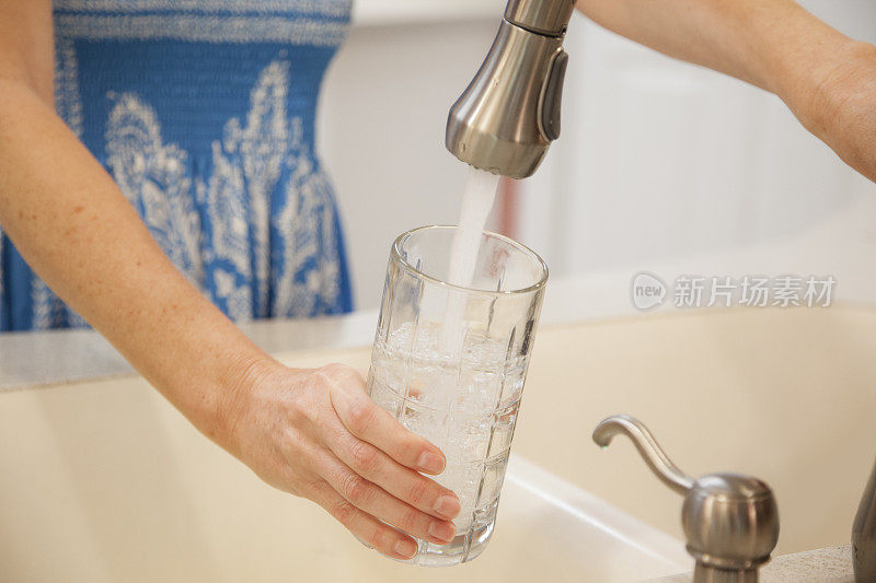 女人可以喝到装在玻璃杯里的清水。厨房的水槽。