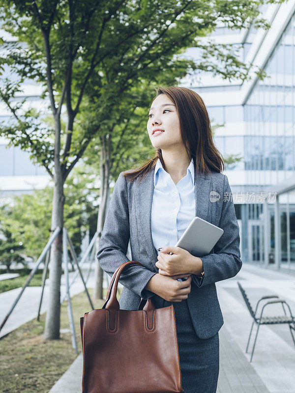 漂亮的亚洲女孩拿着平板电脑走出办公楼