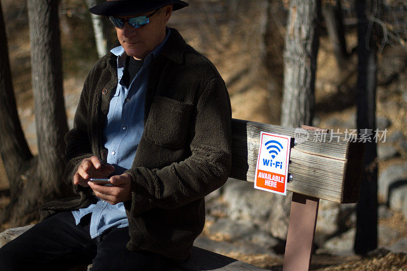 在“这里有Wifi”标志附近的树林长椅上的男人