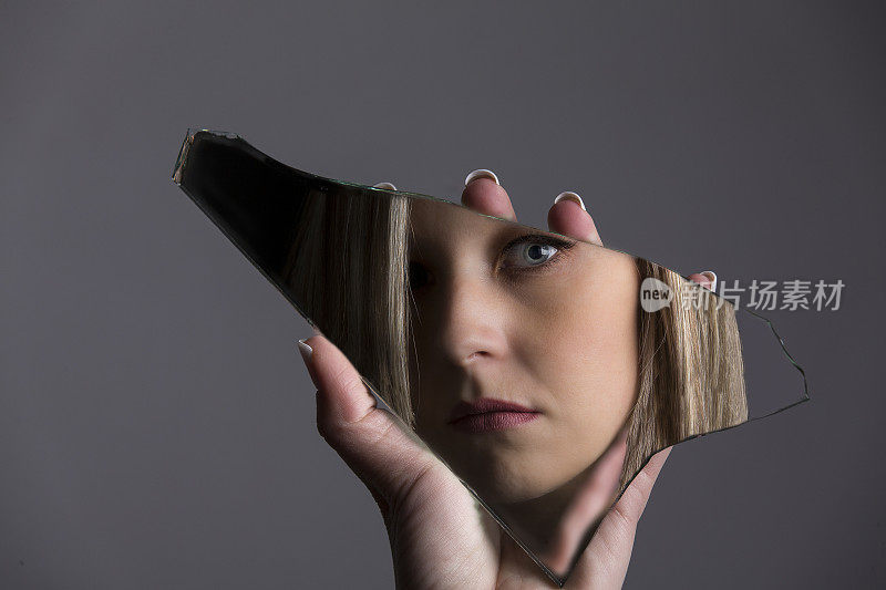 一个女人看着自己的脸在破碎的镜子碎片里