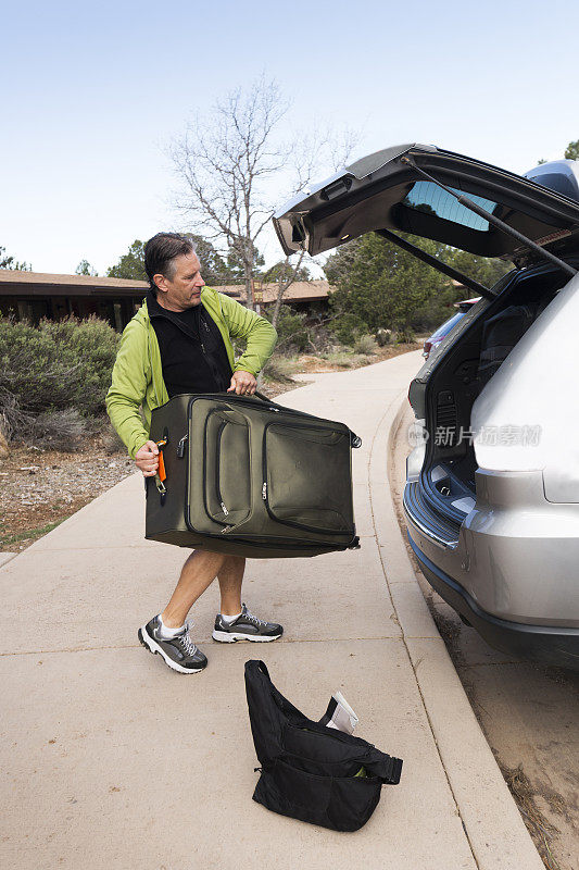 一名成年男子在穿越美国亚利桑那州的公路旅行中提着一个箱子准备放进汽车后备箱