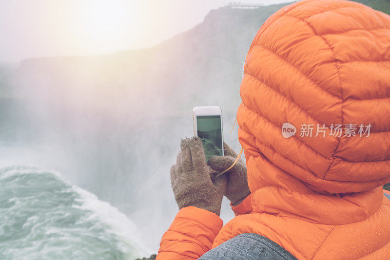 一名年轻女子在冰岛瀑布边用手机拍照