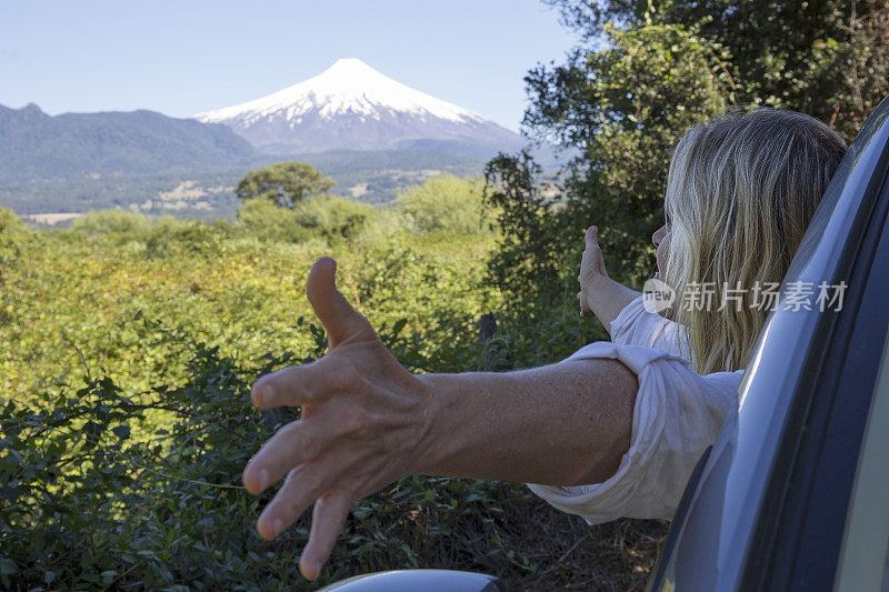 女人从车窗探出身子，向火山伸出双臂