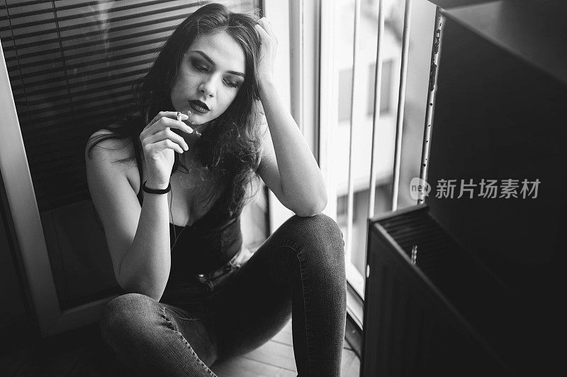 一个戴着耳机的女人坐在窗边抽烟。黑色和白色。