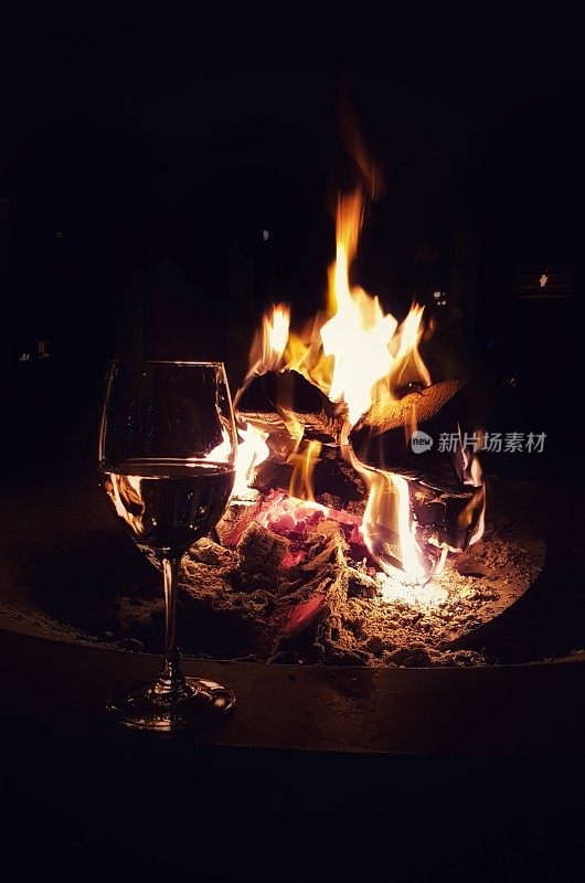 背景是燃烧着的壁炉的白葡萄酒杯