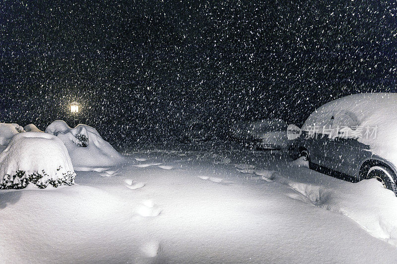 脚印和停在夜晚的汽车车道上覆盖着厚厚的暴风雪